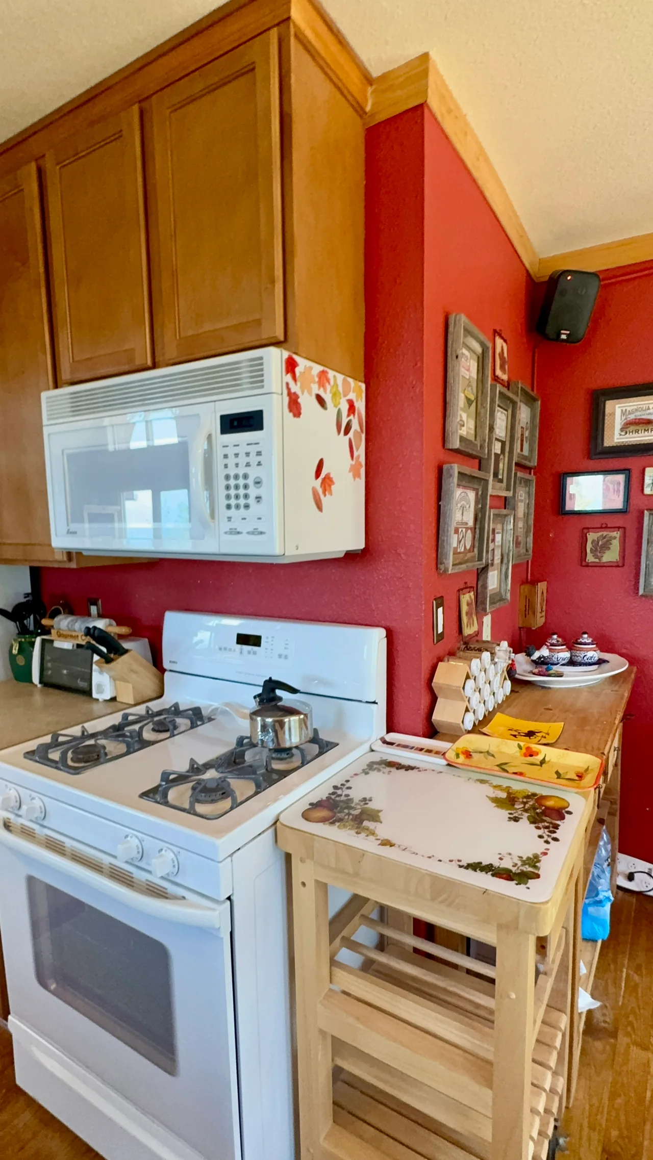 White gas range and microwave beneath wooden cabinets, with a narrow kitchen work surface beside a red wall.