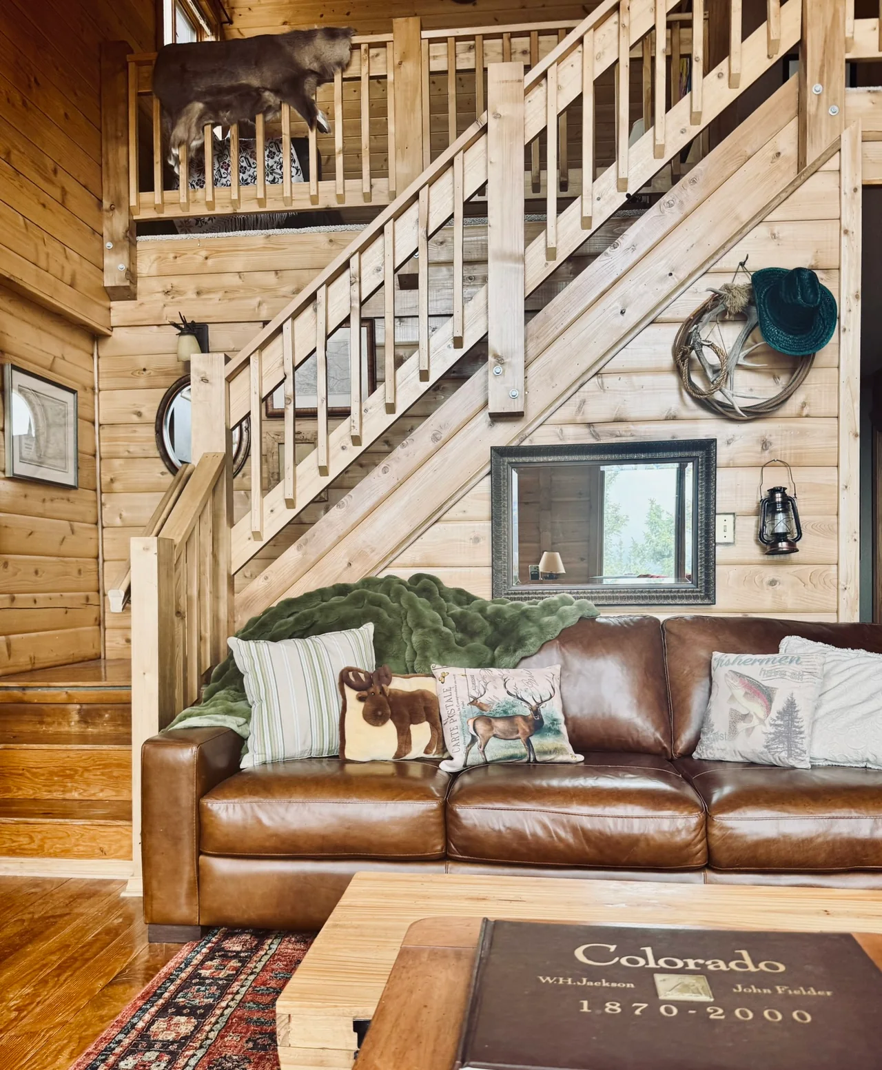 Brown leather sofa with patterned cushions beneath a wooden staircase in the wood-paneled living room.